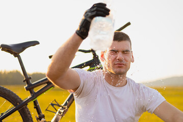 Tired cyclist refreshes splashing water on his face from a bottle after riding bike during the hot...