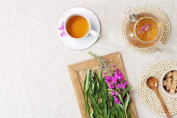 Fireweed tea in white cups and transparent glass teapot, herbal hot tea from green leaves of ivan chai on textile tablecloth. Top view healthy drink and wild flowering willow-herb, tea time