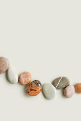 Aesthetic minimal flat lay with sea pebble stones on beige background with copy space. Row from natural smooth stone pastel color and sardonyx gemstone. Summer concept, top view