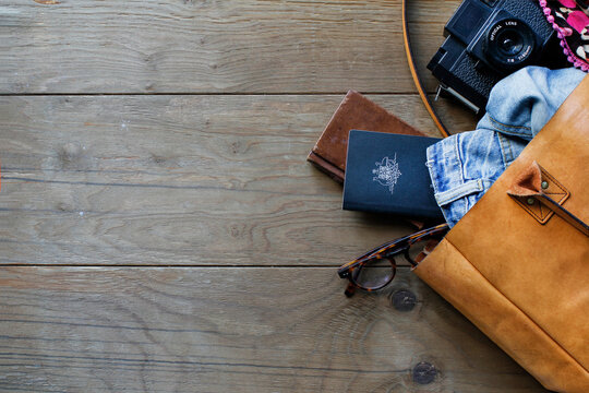 Tan leather tote bag with travel items on wooden floor