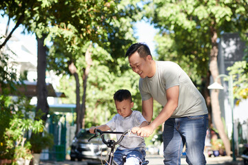 Naklejka na ściany i meble Happy dad teaching kid how to ride bicycle on sunny day