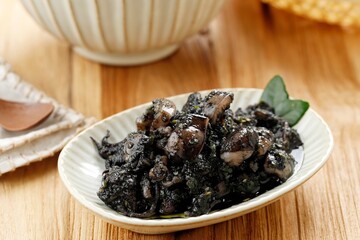 Fototapeta na wymiar Stir Fried Squid and Chili in Black Squid Ink Sauce Served in Ceramic Plate. Known as Tumis Cumi Hitam Pedas In Indonesia.