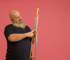 a man with a beard in a black t-shirt repairs a crutch with his finger, colored background with...