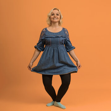 pretty blond bbw woman in a blue dress makes a curtsey on a colored background