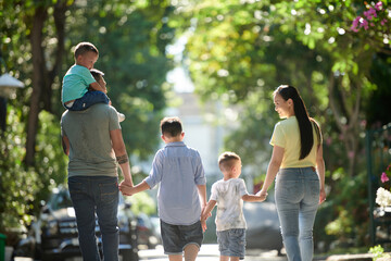 Happy family of five walking in street together on sunny day, view from behind