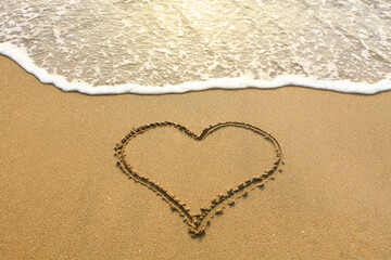 A heart-shaped painting on a sandy beach with a wave at sunset. Communication to lovers. 
