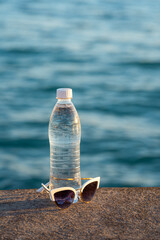 beautiful summer background with a bottle of drinking water and sunglasses and the sea in the background
