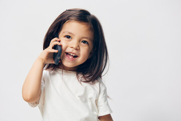 a little girl of preschool age, sitting on a white background in a white T-shirt, enthusiastically...