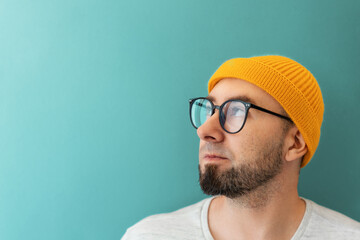 Portrait of a Caucasian young bearded man with glasses and a hat looking at the left side. Copy...