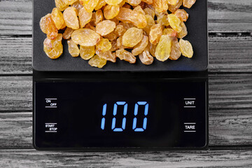 yellow raisins on an electronic kitchen scale. On a digital scale displaying 100 grams.