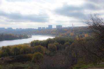 Obraz premium City park in autumn, river bend, yellowing deciduous trees and high-rise residential buildings, photo defocus soft focus