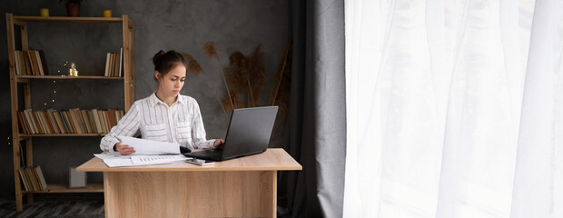 young brunette working at her office desk with documents and laptop. Businesswoman working on...