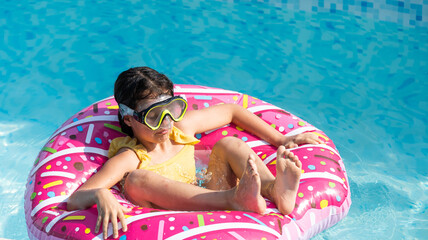 Cute little girl in a bathing suit lying on a donut inflatable circle. The child swims on a blue...