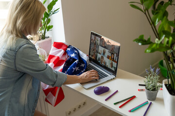 Happy young female student hold flag of USA, studying with laptop with blank screen in living room interior. International education at home, lesson remote, website due covid-19 quarantine