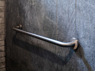 Close-up photo of stainless steel grab bar handrail installed on grey stone tiles wall background in a hotel handicapped disabled access bathroom. - obrazy, fototapety, plakaty