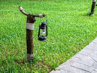 Old vintage street lamp on the wooden pole near the stone walkway and green grass, outdoor yard...