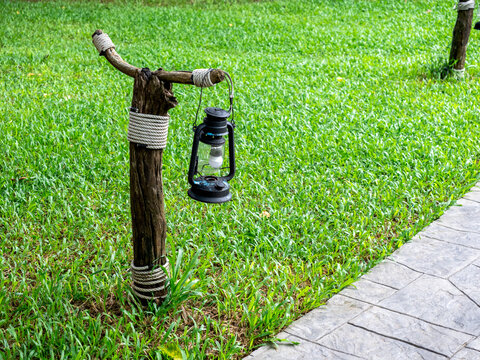 Old vintage street lamp on the wooden pole near the stone walkway and green grass, outdoor yard with copy space.