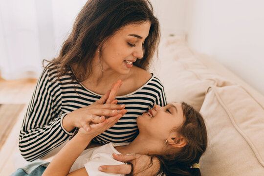 Horizontal picture of beautiful brunette female in striped blouse singing to her preteen charming girl, lying in her hands, showing her love and care. Warm human relationships. Conscious maternity