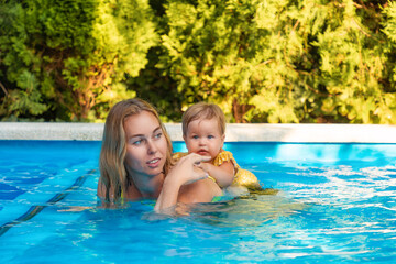 Fototapeta na wymiar Portrait of young woman instructor swimming in the pool with her little girl