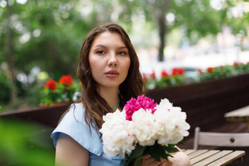 A beautiful young woman in a blue dress with a bouquet of peonies.