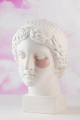 Hydrogel pink patches on the plaster head of Aphrodite on a pink background. Beauty concept.