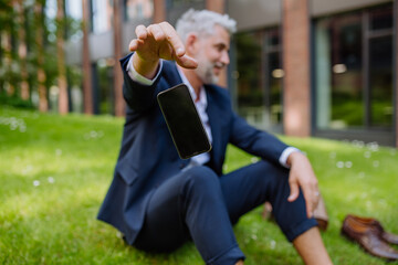 Mature businessman throwing away his smarthpone when sitting barefoot in park, feeling free,...
