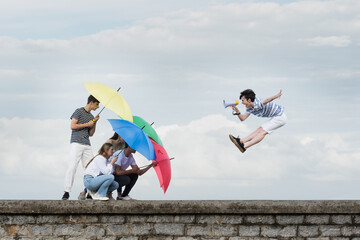 Abstract concept of ignoring toxic comments. Teenager boy shouting on megaphone and friends protecting themselves using umbrellas.
