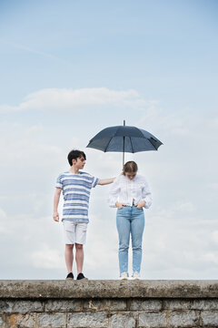 Abstract concept of support to sad person. Teenager boy holding umbrella and covering girl. Depression and mourning help concept.