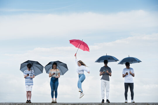 Teenager girl celebrating freedom from social media. Young woman holding red umbrella standing out from crowd. Overcoming digital addiction concept.