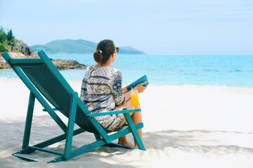 Woman with book sits in sun lounger on beach and looks at sea on sunny day.