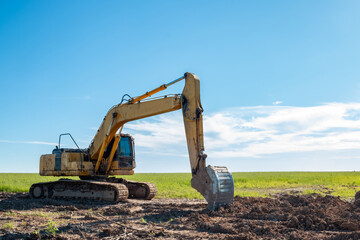 Excavator on the background of a green field.