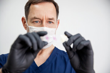 doctor in black gloves and white mask holds stained histology slide which is ready for microscopic...