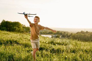 Ginger boy playing toy airplane on the meadow