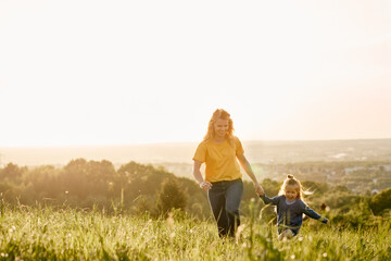 Caucasian mom with daughter running at the meadow