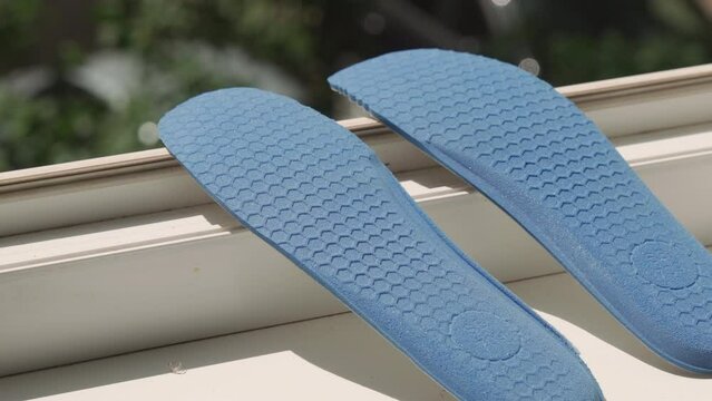 Blue shoe insoles dry on the windowsill in the sun. Close-up, slow camera movement back.