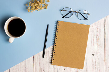 Working space with glasses, flowers, coffee, notebook and pen over the blue and wooden background. 