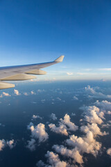 Fototapeta premium Fluffy clouds outside airplane window with view of airplane wing