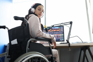 Female freelancer programmer or streamer in modern headphones sits in wheelchair and uses computer