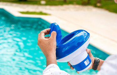 Hands of a worker installing a pool chlorine float, a person holding a pool chlorine dispenser....