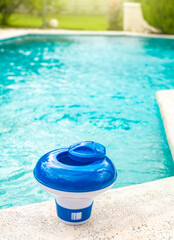 A chlorine float on the edge of a swimming pool. A chlorine dispenser for swimming pools with blue...