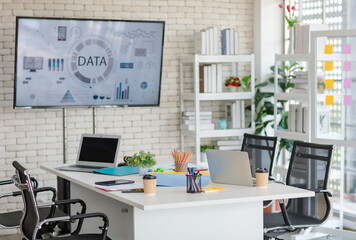 Modern decorated office workstation meeting room in company with desk full of stationary equipment, black blank screen mockup laptop notebook computer, tablet, pencils, plant pot, post it and folders