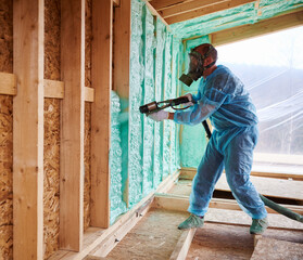 Male builder insulating wooden frame house. Man worker spraying polyurethane foam inside of future cottage, using plural component gun. Construction and insulation concept. - obrazy, fototapety, plakaty