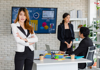 Portrait shot Asian young happy cheerful confident millennial professional successful female businesswoman in formal suit sitting crossed arms smiling while colleagues working in blurred background.