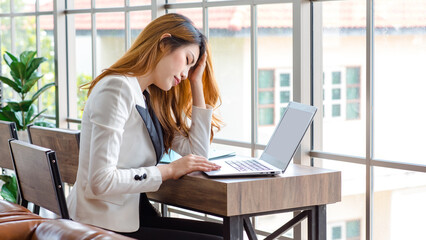 Closeup shot of upset stressed depressed worried unhappy Asian millennial frowning face businesswoman employee sit holding hands on head while working with laptop notebook computer in company office.