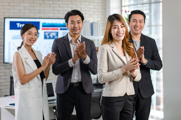 Group of Asian happy cheerful millennial professional successful male businessmen and female businesswomen in formal suit standing clapping hands applauding greeting celebrating together in office