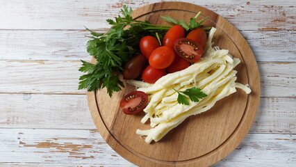 String cheese or cheese whip - salty snack cheese with cherry tomatoes and herbs on chopping board. Turkish cheese