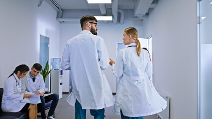 Fototapeta premium Good looking lady doctor and the guy nurse have a discussing in the hospital corridor they analyzing the diagnostic of the patient background other doctor sitting on the chair