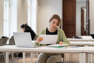Focused hard-working middle-aged female student reading architectural drawings, working on...