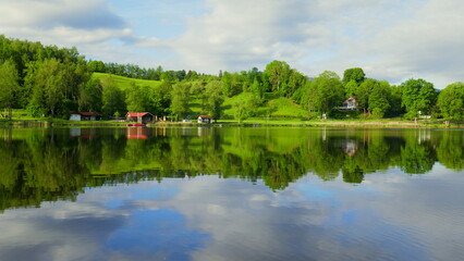 Fototapeta na wymiar Blick über spiegelnden Bad Soier See mit grüner Landschaft und weißen Wolken bei blauem Himmel