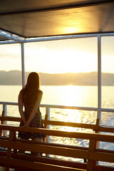 Long hair young woman staying on the deck of the ferry and looks at the sunset.